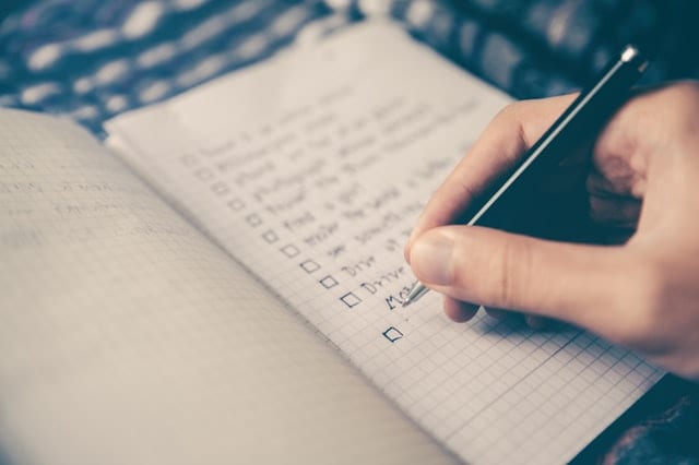 a hand holding a pen writing out a checklist in a small notebook