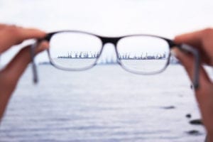 two hands holding glasses with a harbor cityscape viewed in the distance