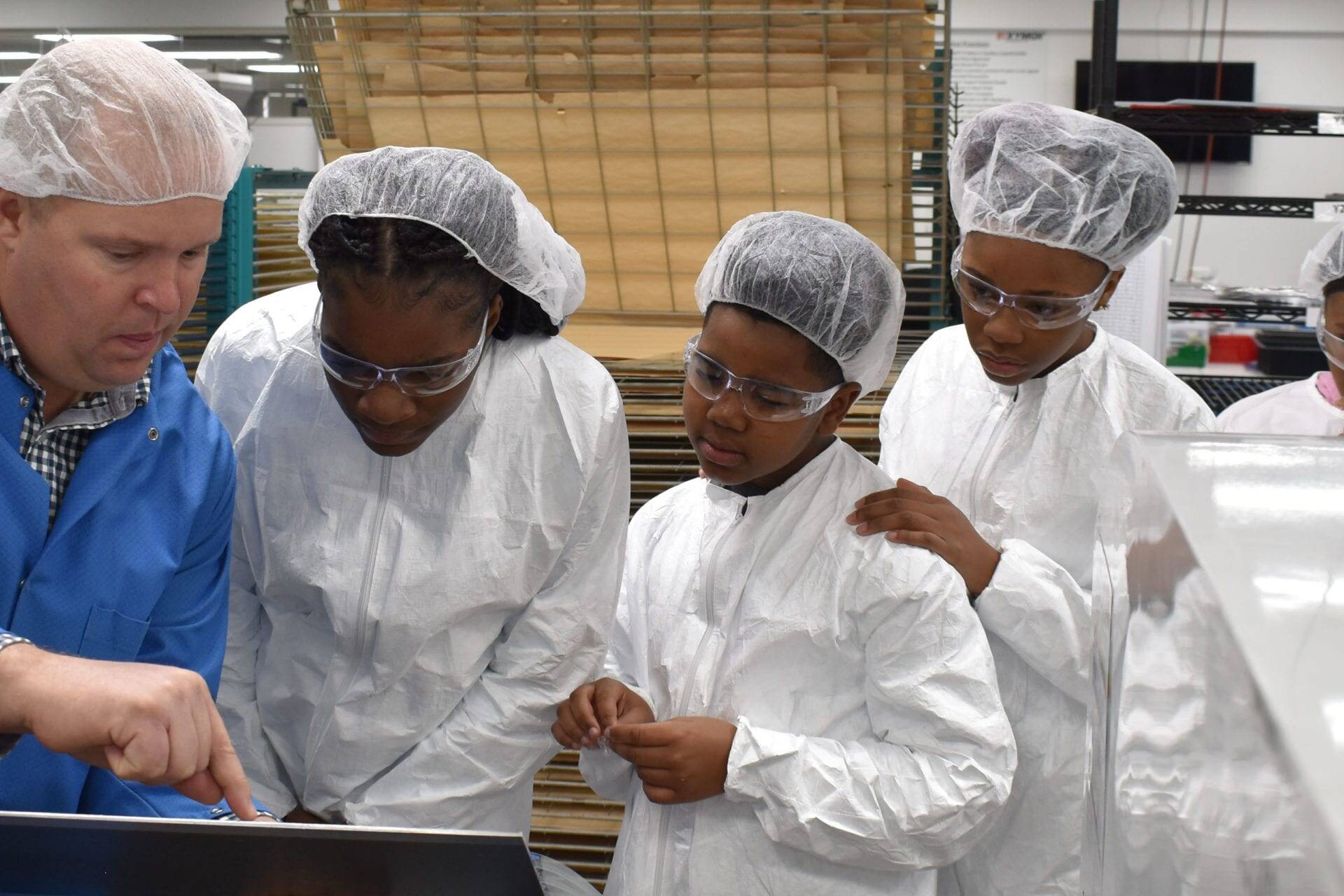 five people gathered around a touchscreen in a production facility, all wearing lab coats and hairnets