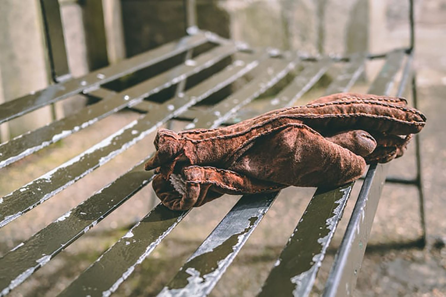 brown pair of worn gloves sitting on a metal park bench with peeling paint