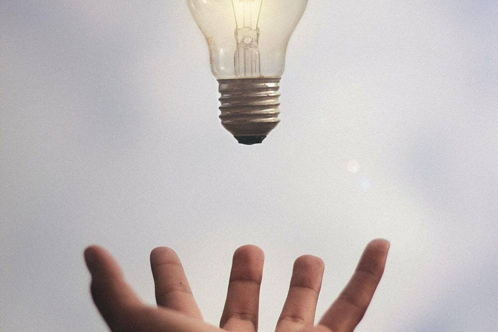 a lit light bulb falling into an open hand