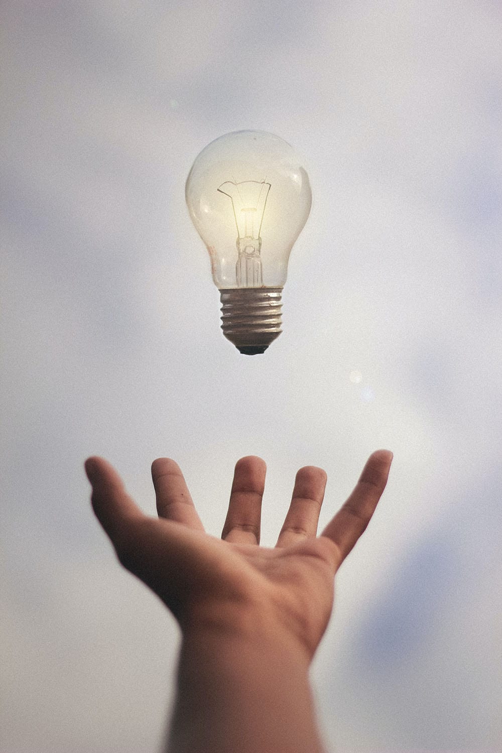 a lit light bulb falling into an open hand