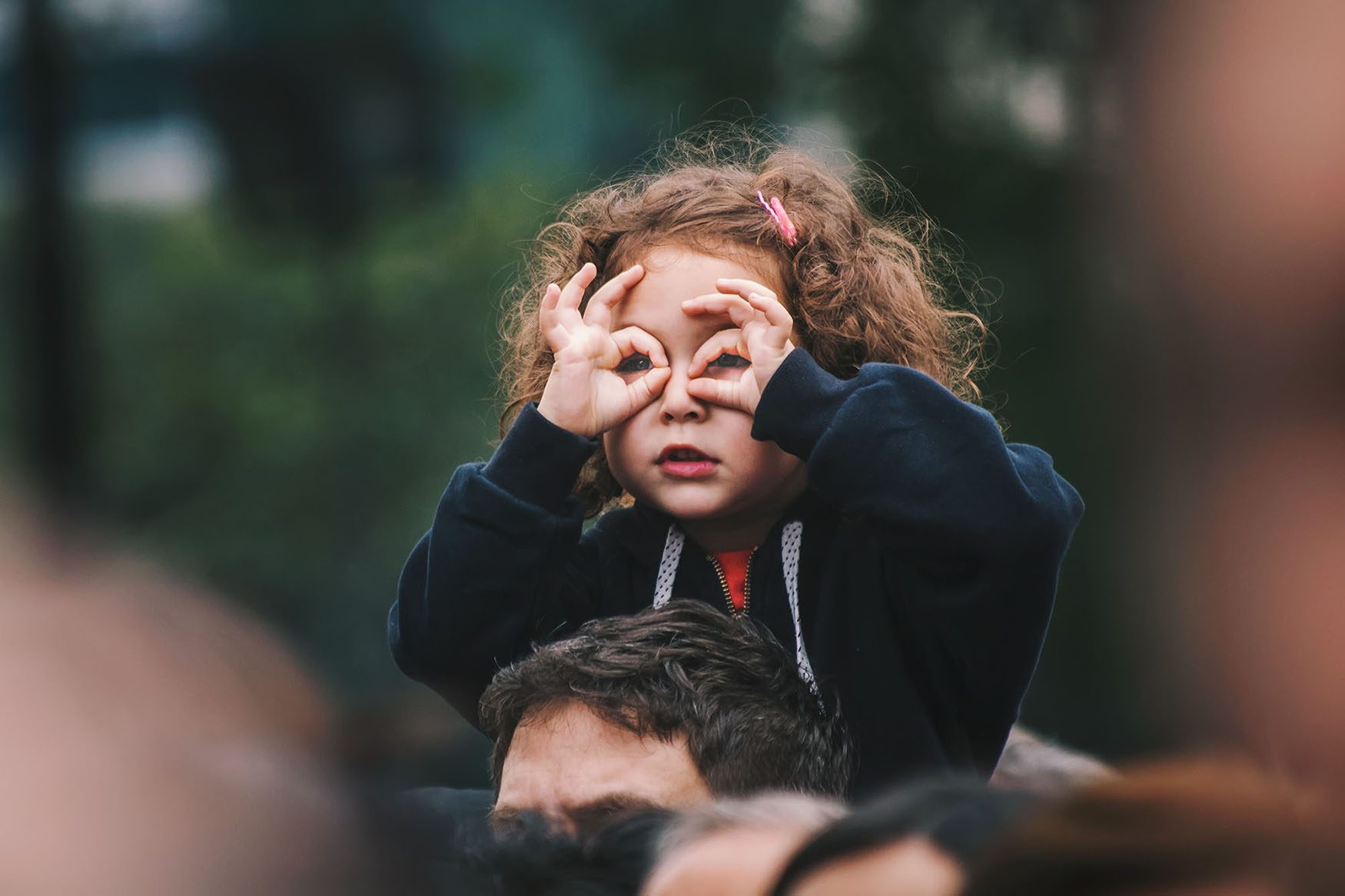 little girl on a man's shoulders looking through her finger glasses