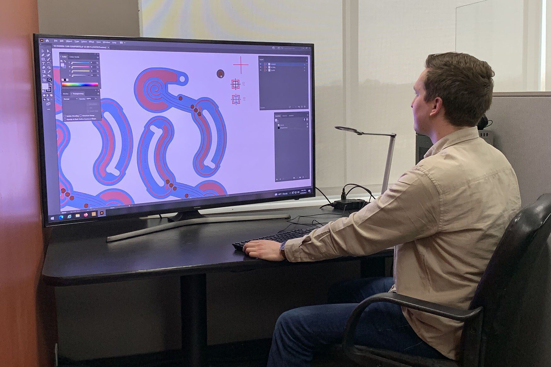 person working at a desk looking at a large monitor and doing CAD programming