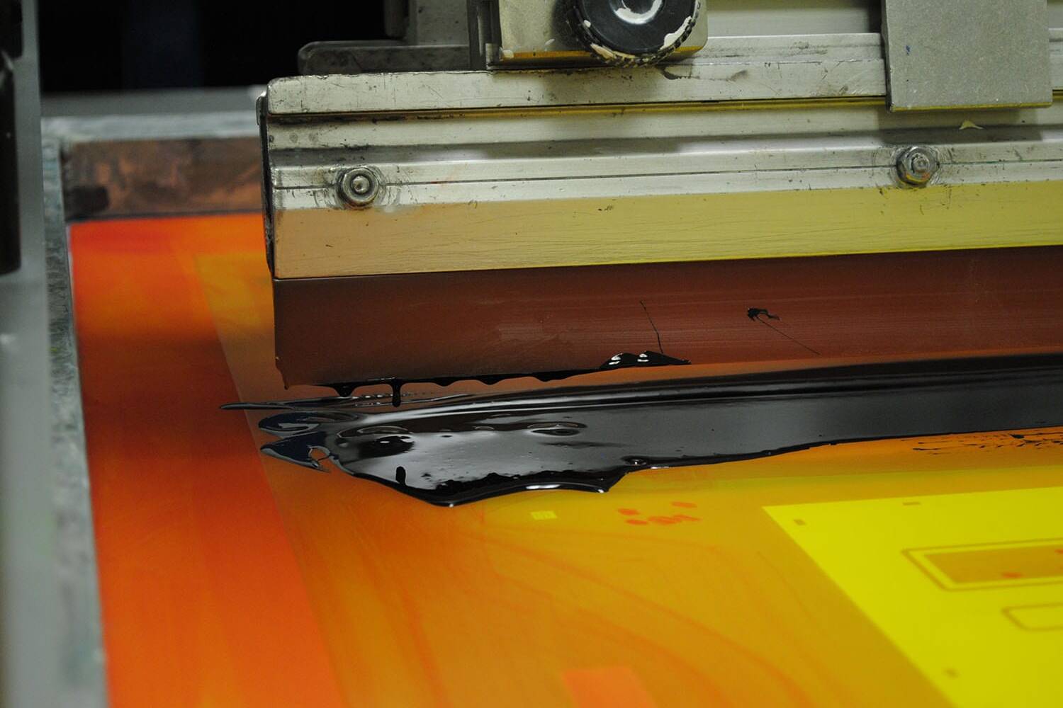 a screen printing machine spreading black ink across an orange panel