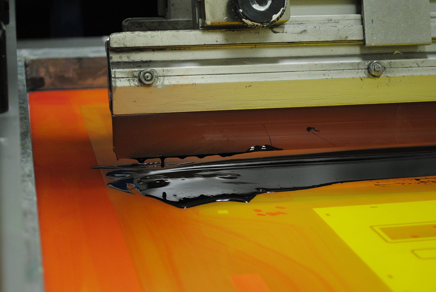 a screen printing machine spreading black ink across an orange panel