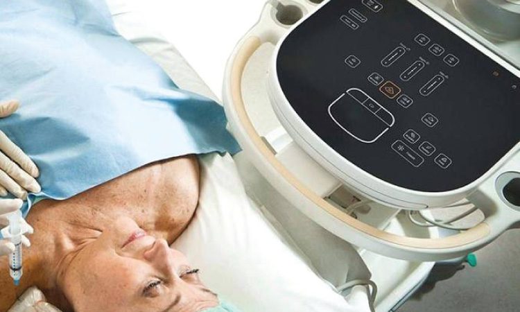 woman laying on a table in a medical facility next to a piece of equipment featuring several haptic touch buttons