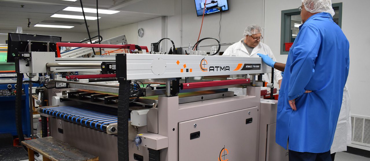 two employees in blue and white lab coats and hairnets working with equipment in a production facility