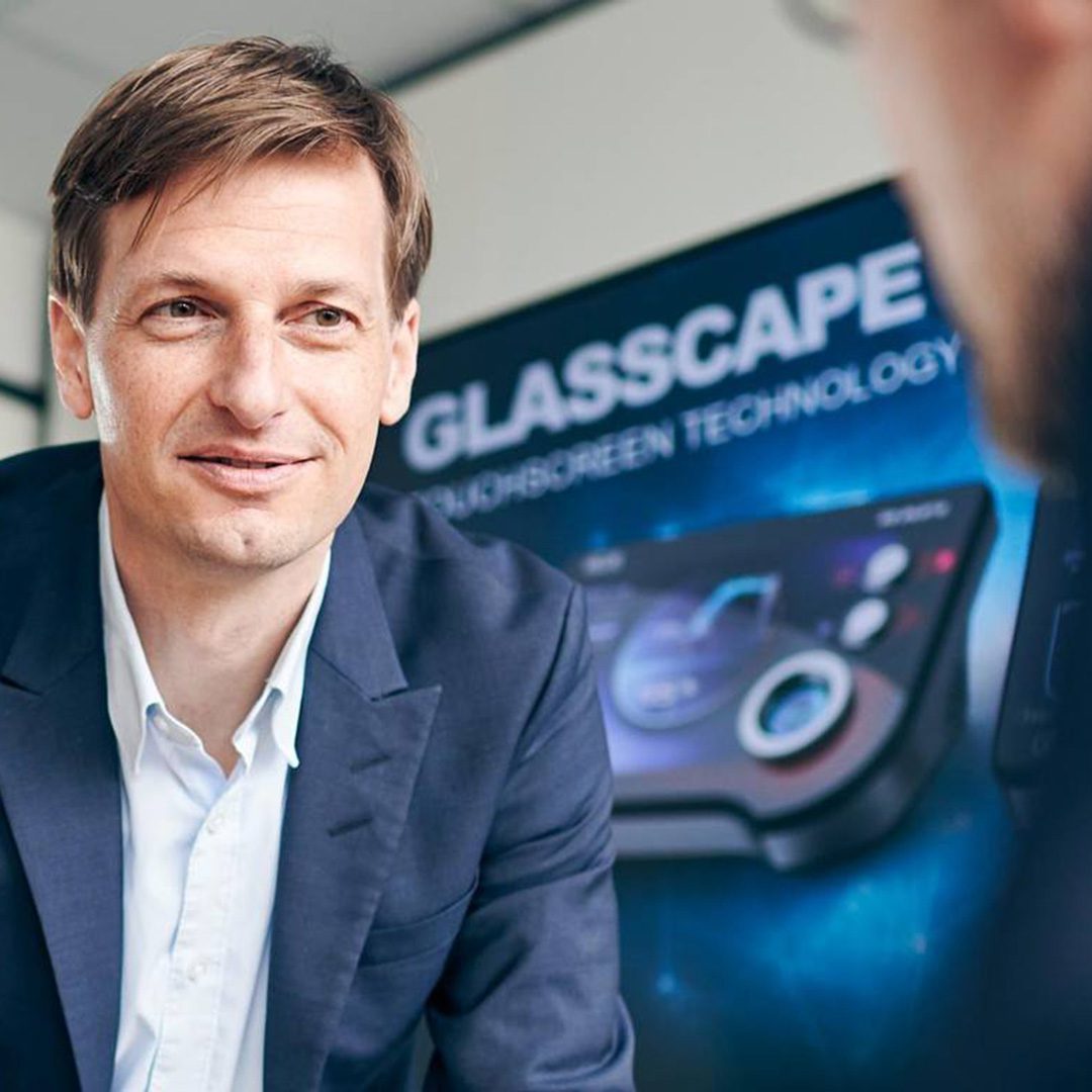 a man talking to someone with a banner of the GLASSCAPE technology in the background