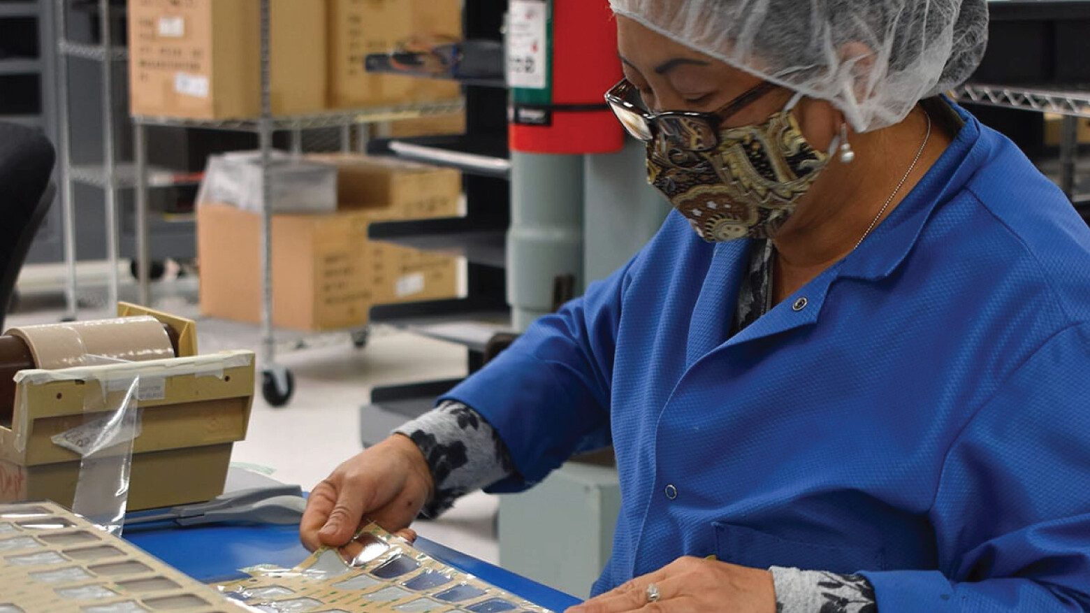 female Xymox employee with glasses and wearing a hairnet and lab coat working with printed technology in a production facility